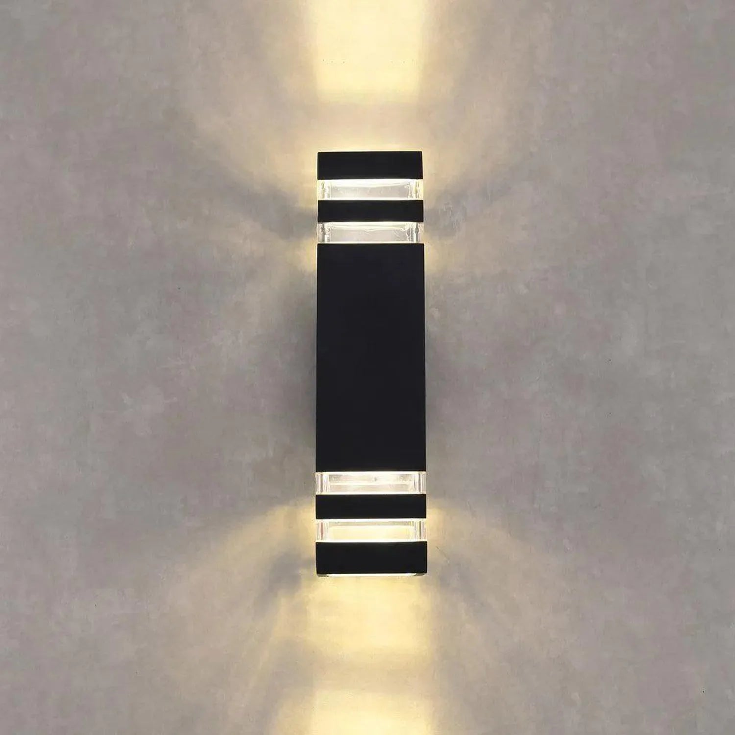 Black cylindrical LED wall light mounted on white wall, glowing with warm white light radiating upward and downward.