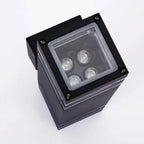 Black square LED outdoor wall light with four illuminated bulbs visible through transparent cover, mounted on light gray exte