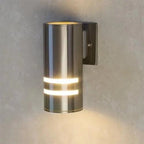 Cylindrical stainless steel wall sconce with two horizontal light bands, mounted on gray wall, lit to show warm glow.