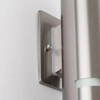 Stainless steel rectangular wall-mounted light fixture installed on white wall next to metal downspout, shown in installation