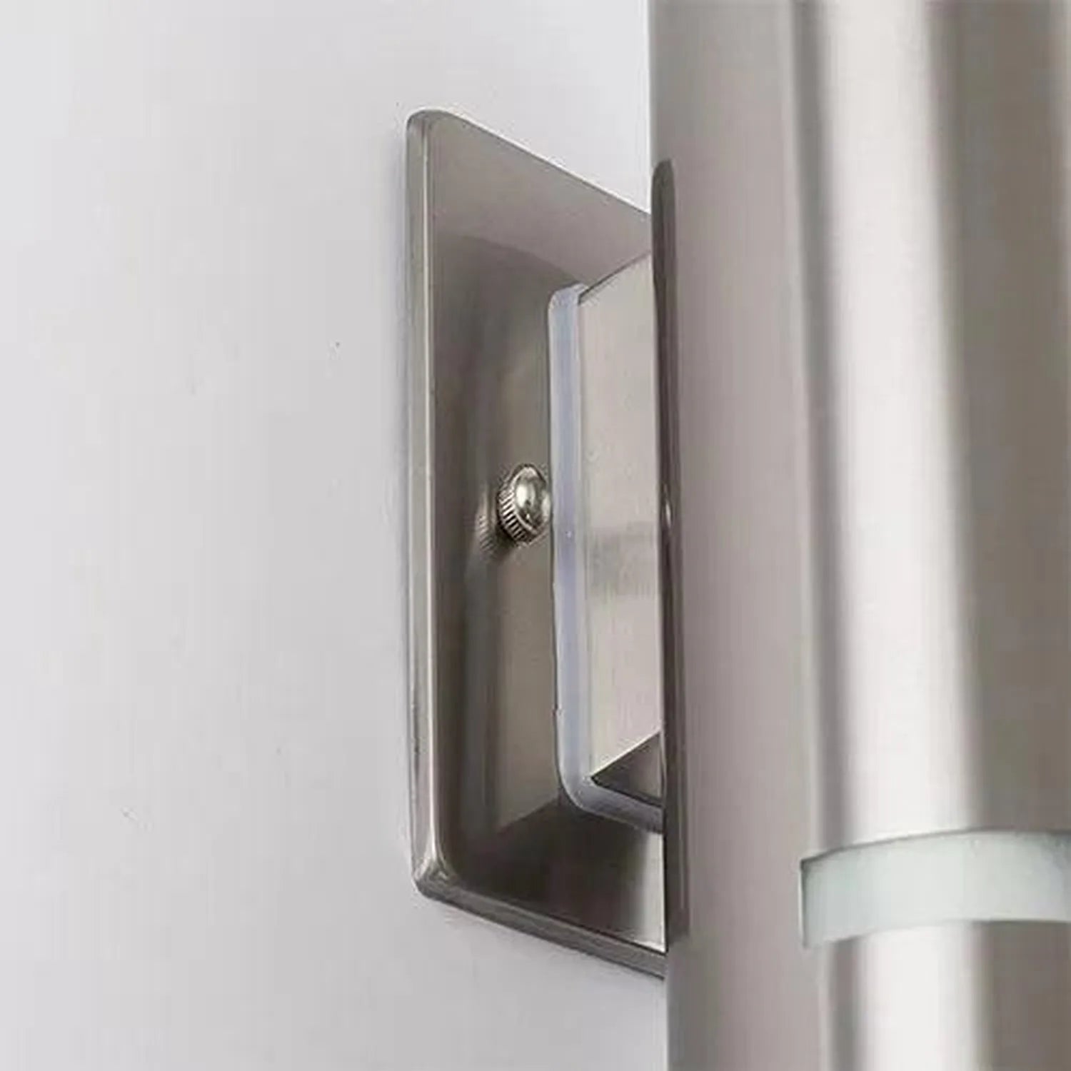 Stainless steel rectangular wall-mounted light fixture installed on white wall next to metal downspout, shown in installation