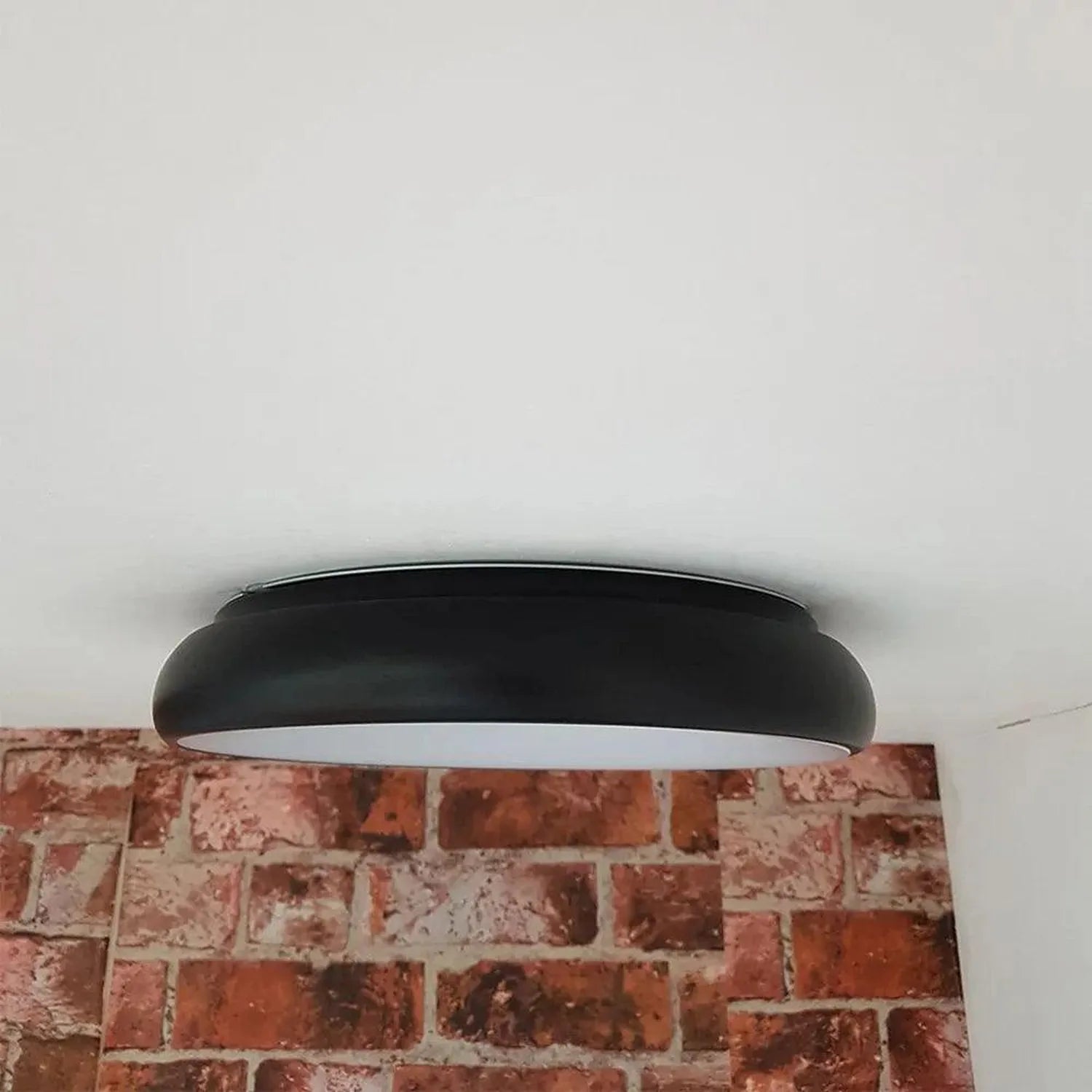 Black oval LED ceiling light mounted on brick wall against white ceiling, installation shot.