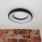 Black and white round LED ceiling light mounted on white ceiling above brick wall.