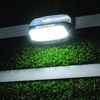 Solar LED wall light mounted on fence at night, illuminating green foliage below with bright white light.