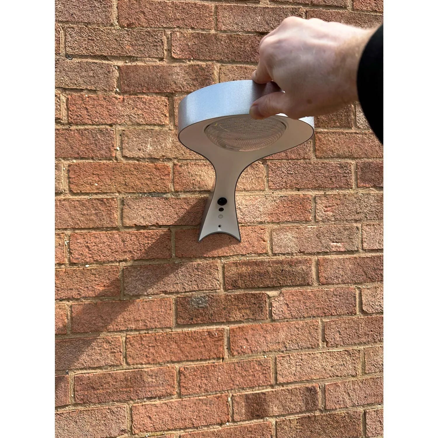 Hand holding white solar wall light with heart-shaped design against brick wall, installation shot.