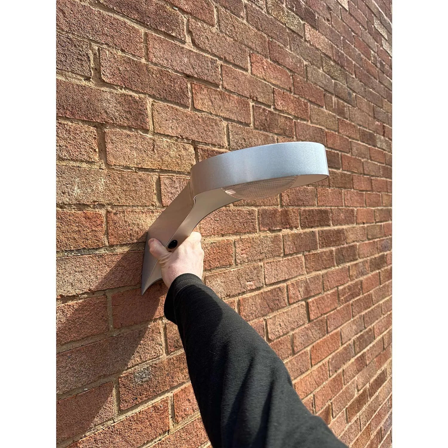 Solar LED wall light mounted on brick, installed horizontally with motion sensor visible, being held at hand level for demons