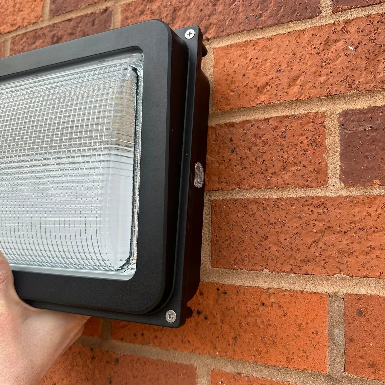 Black rectangular LED wall pack light mounted on red brick exterior wall, installation shot.