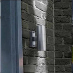 Stainless steel cylindrical wall light mounted on dark brick wall, showing twin pack installation shot with lighting effect.