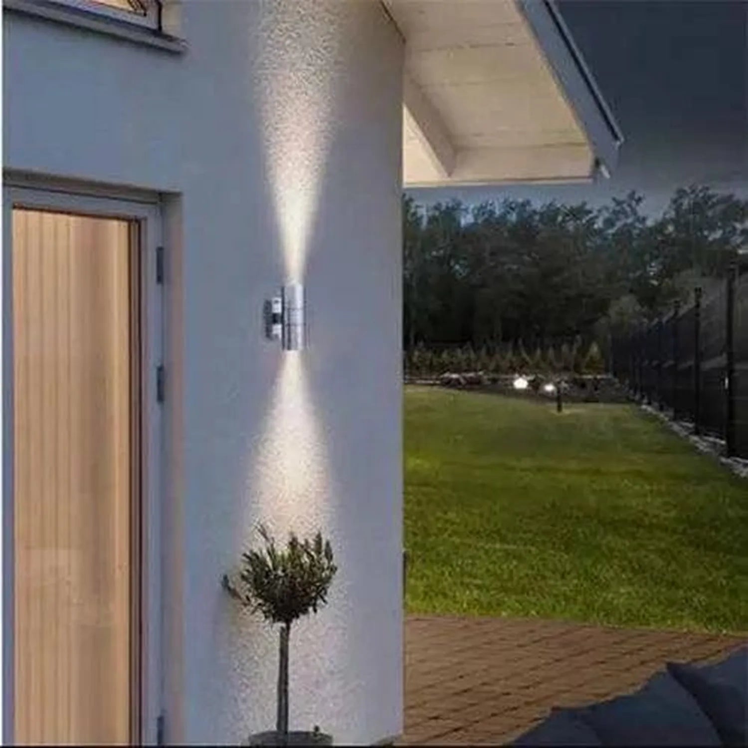 Modern stainless steel outdoor wall lights illuminating a contemporary white house exterior at dusk, with manicured lawn and 