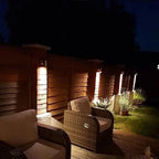 LED outdoor spotlights illuminating modern wooden fence and rattan patio furniture at night.