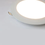 Slim white round LED panel light installed in ceiling, glowing brightly with visible power cable connector.