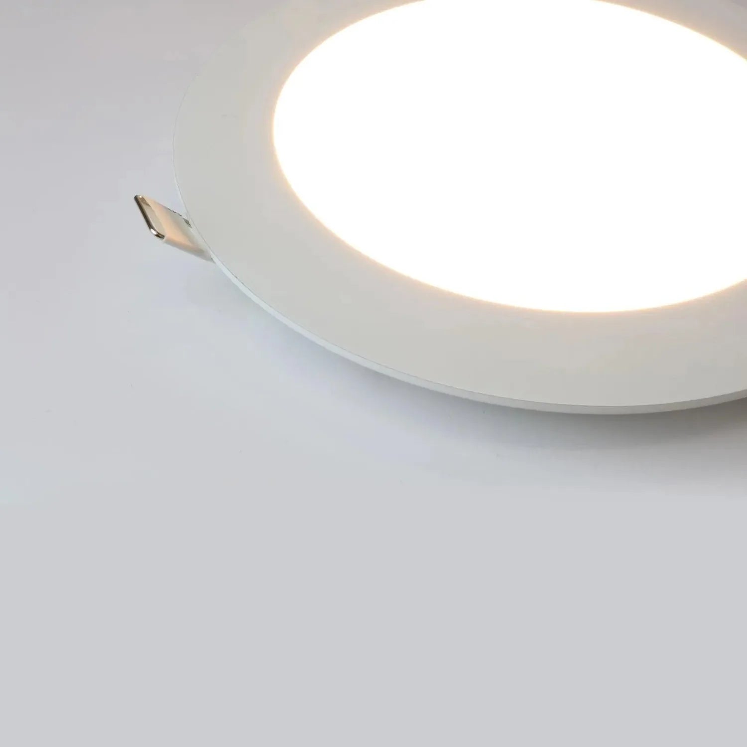 White round recessed LED panel light installed in ceiling, emitting bright white light with visible mounting bracket.