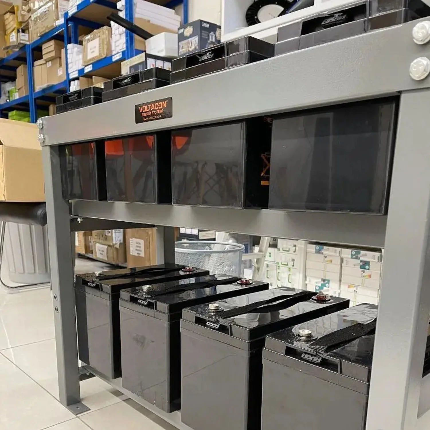 Voltagon 48V gel battery bank display with four units mounted on steel racks in warehouse setting, showing product labeling a