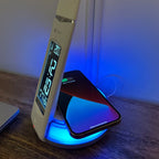 OttLite LED desk lamp with digital clock displaying 20.6 degrees, positioned next to glowing blue wireless charging pad holdi