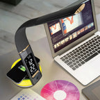 OttLite LED desk lamp with yellow base and black curved shade, displaying clock, next to laptop and wireless charging pad.