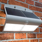 White solar LED wall light mounted on red brick, showing curved top panel with dark solar cells and white light-emitting sect