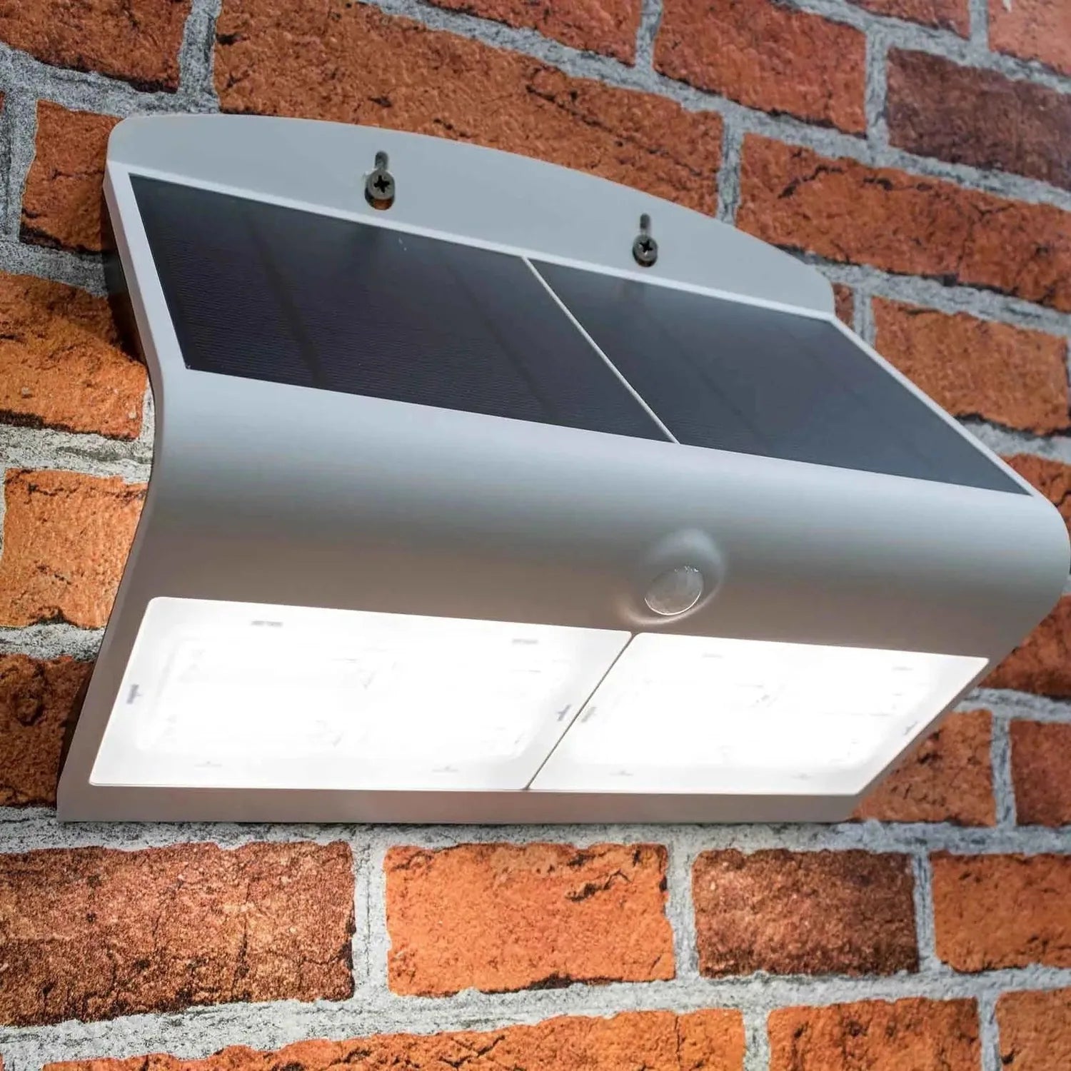 White solar LED wall light mounted on red brick, showing curved top panel with dark solar cells and white light-emitting sect