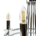 Two LED filament bulbs displayed next to a chrome chandelier fixture, showing warm yellow filaments inside clear glass candle