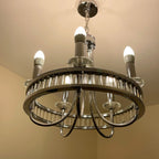Modern chrome chandelier with five lit LED bulbs and crystal prism details, installed on ceiling.