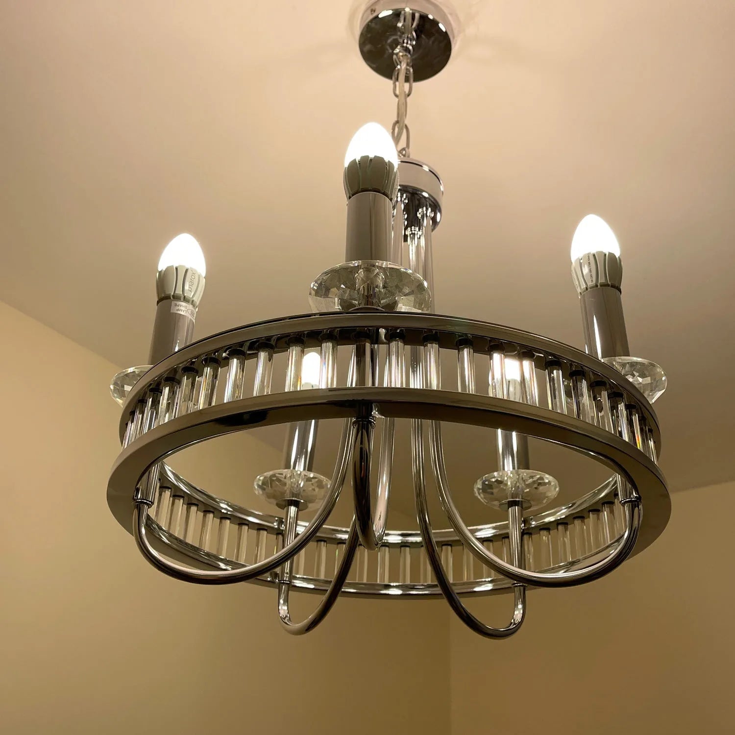 Modern chrome chandelier with five lit LED bulbs and crystal prism details, installed on ceiling.