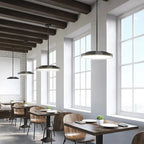 Modern restaurant interior with three black rod-mounted ring pendant lights hanging over wooden tables and chairs near large 