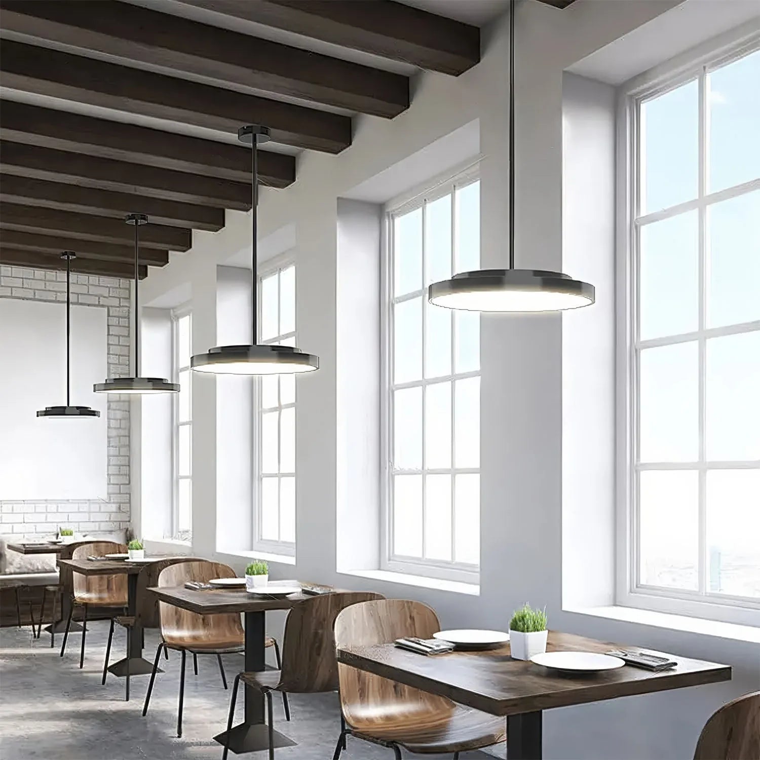 Modern restaurant interior with three black rod-mounted ring pendant lights hanging over wooden tables and chairs near large 