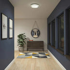Artika Saturn flush mount LED ceiling light installed in modern entryway above dark wooden dresser with plant and round mirro