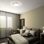 Saturn LED ceiling light installed in modern bedroom, providing warm illumination above bed with dark wood frame and neutral 