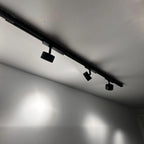 Black track lighting rail mounted on white ceiling with three adjustable spotlight heads casting bright pools of light downwa
