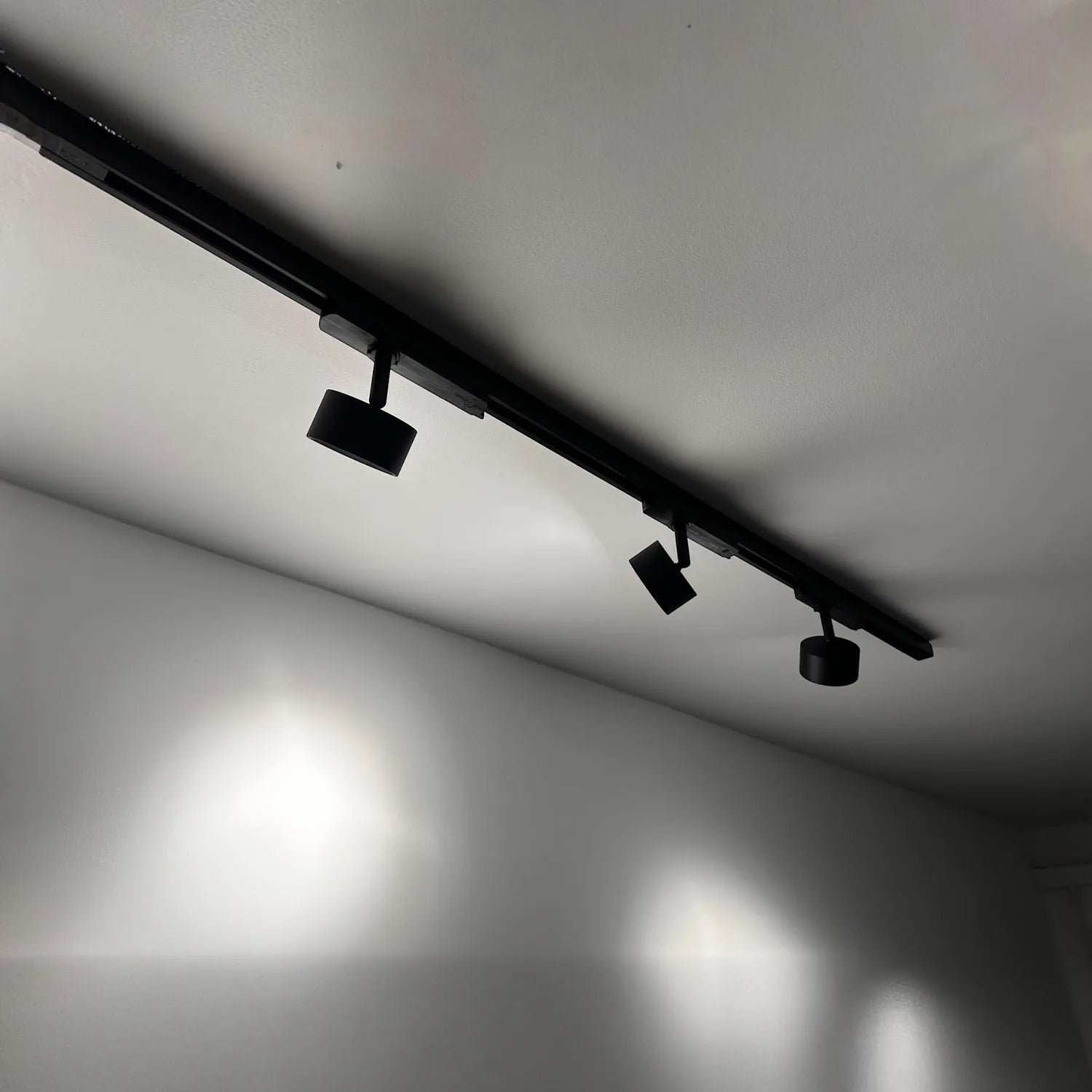 Black LED track lighting system mounted on white ceiling with three adjustable spotlights on one-meter rail.