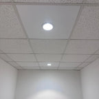 Installed LED downlight with bright white glow in acoustic drop ceiling surrounded by recessed panel tiles in commercial or o