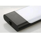 Black cylindrical LED batten light fixture with white diffuser, angled product shot on white surface.