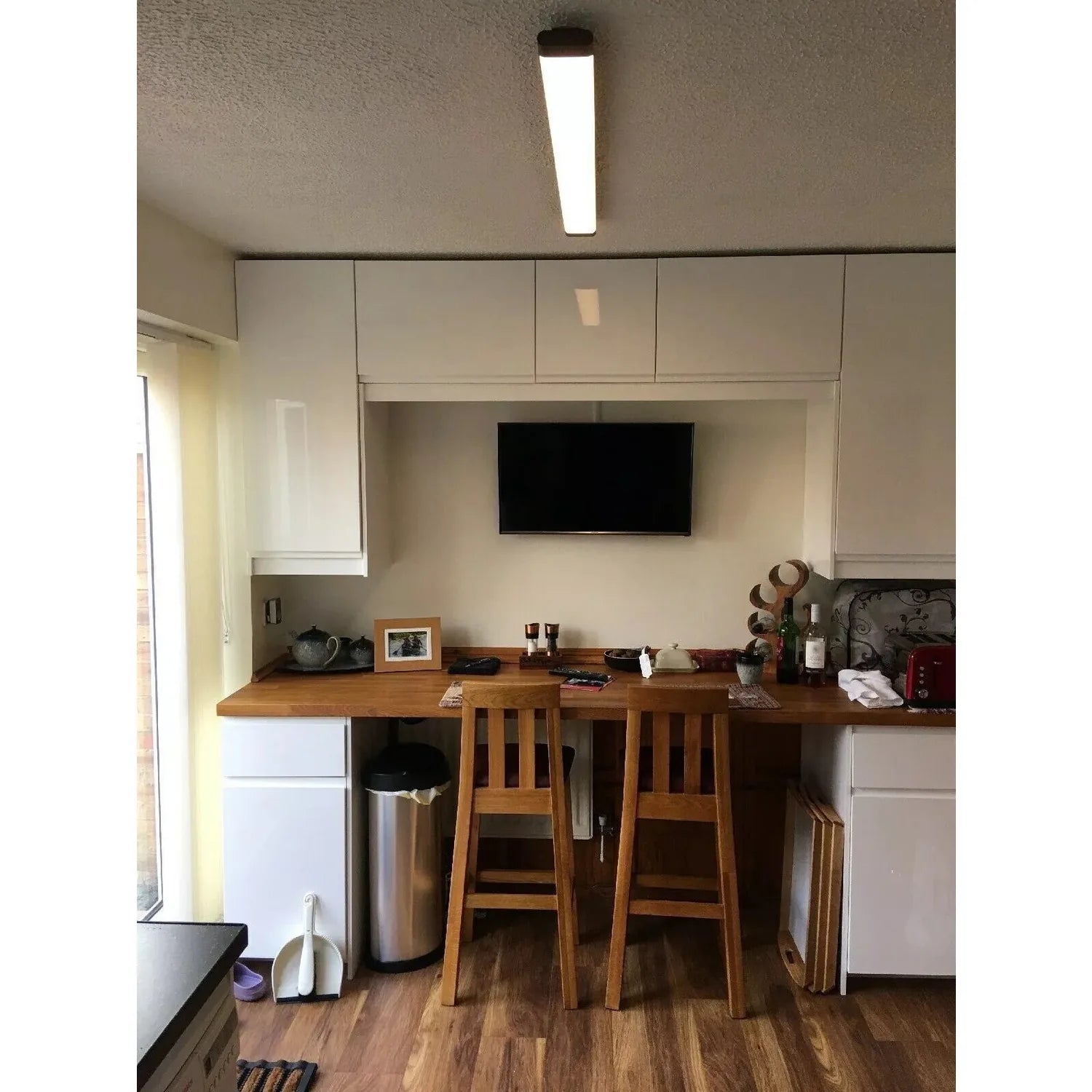 LED batten light installed on kitchen ceiling above counter workspace, illuminating dining area with two wooden bar stools be