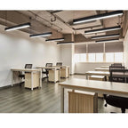 Modern office space with suspended linear LED light fixtures illuminating workstations with wood-grain desk panels and black 