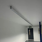 Long linear LED batten light mounted on ceiling above exit door in commercial interior space