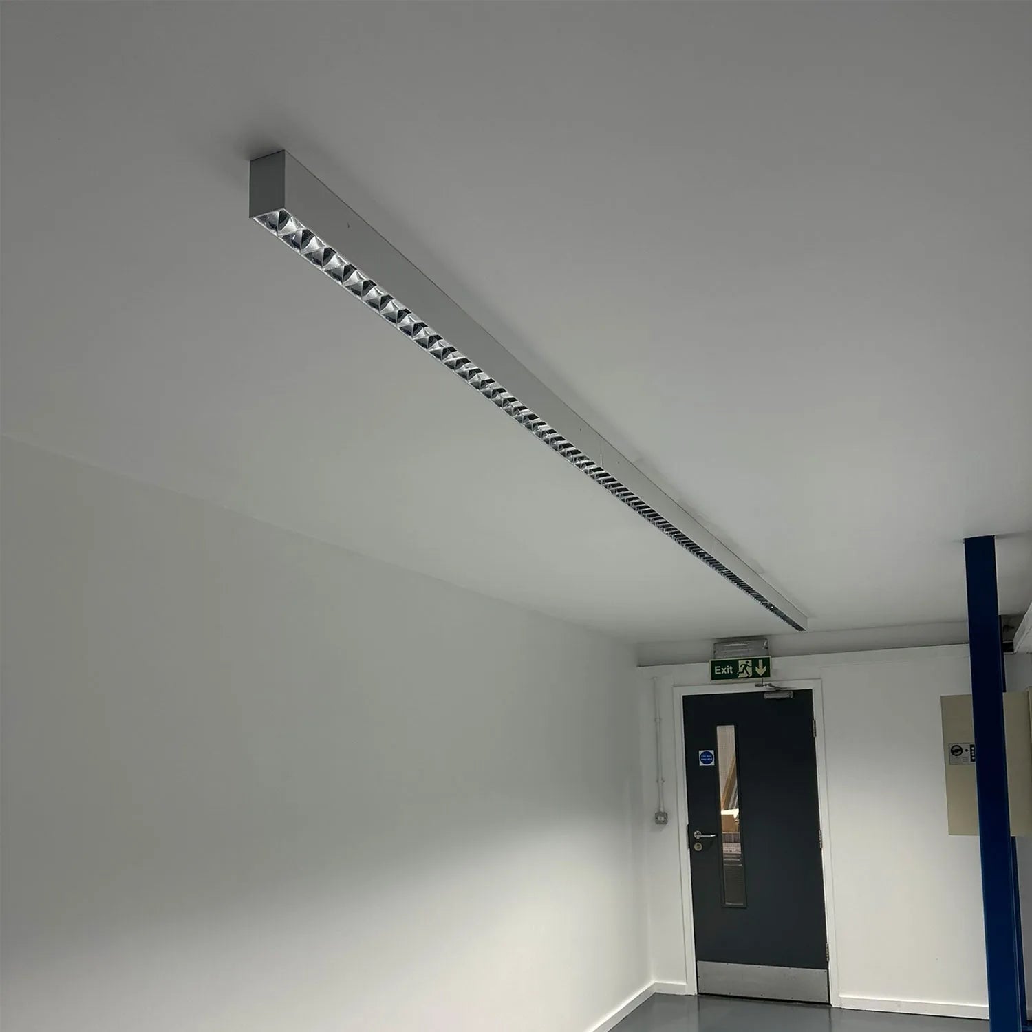 Long linear LED batten light mounted on ceiling above exit door in commercial interior space