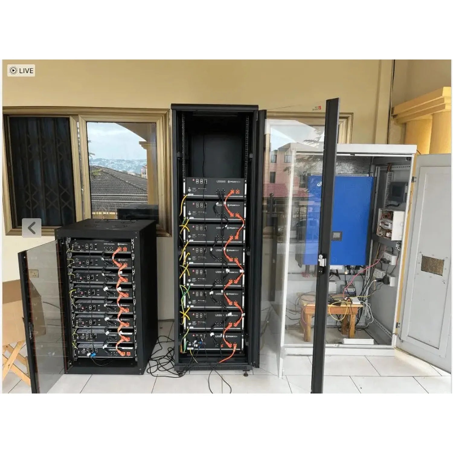 Three Pylontech battery storage units installed in server racks with orange cables and monitoring displays in a bright room w