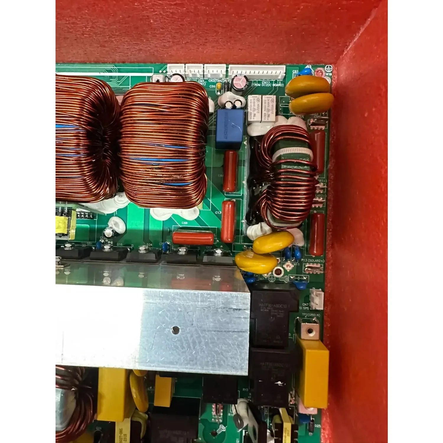 Internal circuit board with copper wire coils, capacitors, and electronic components mounted on green PCB against red backgro