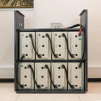 Wall-mounted battery storage system with eight cream-colored battery modules arranged in two rows within a black metal frame,