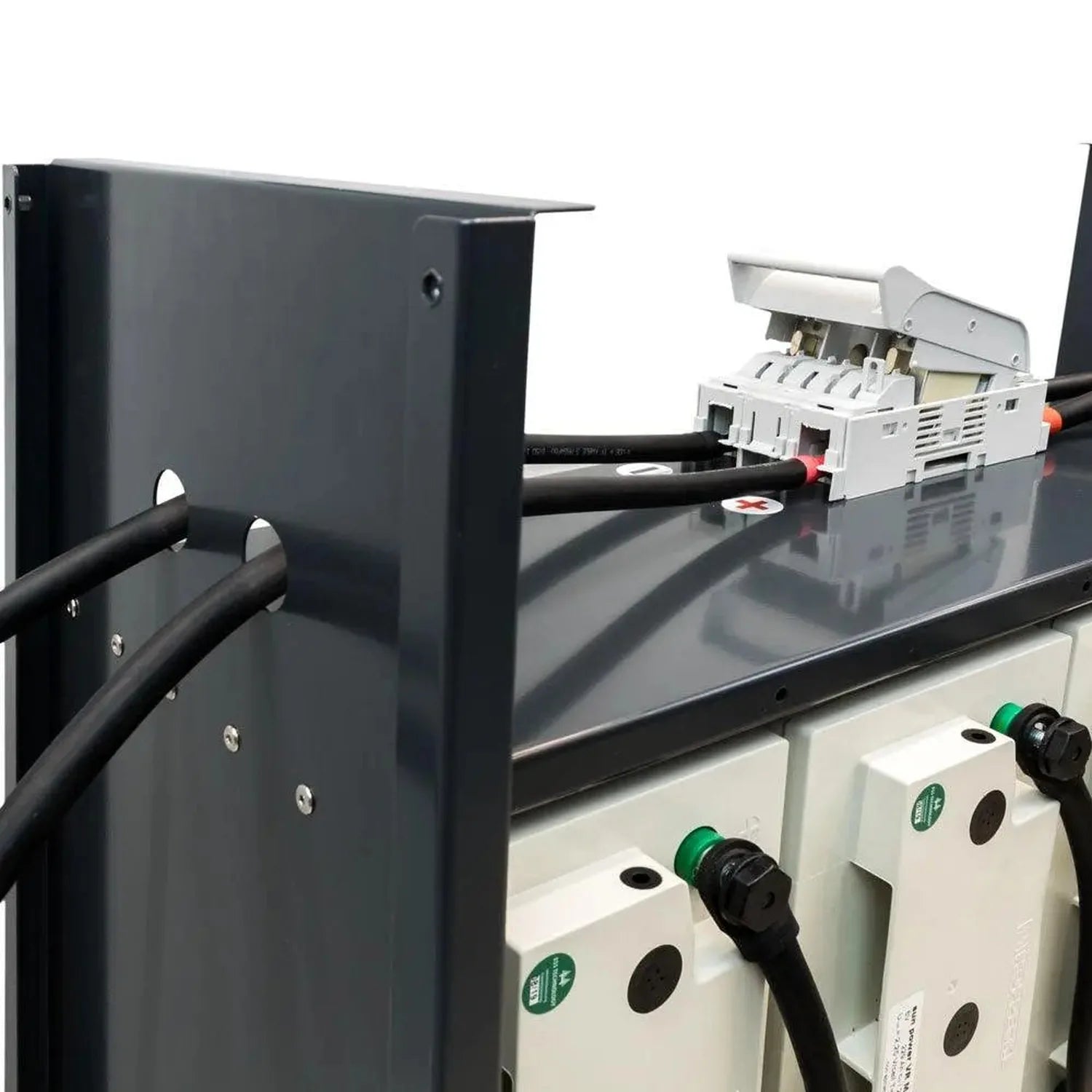 Installation shot of battery storage system with dark metal enclosure, white battery modules, black cables, and green indicat