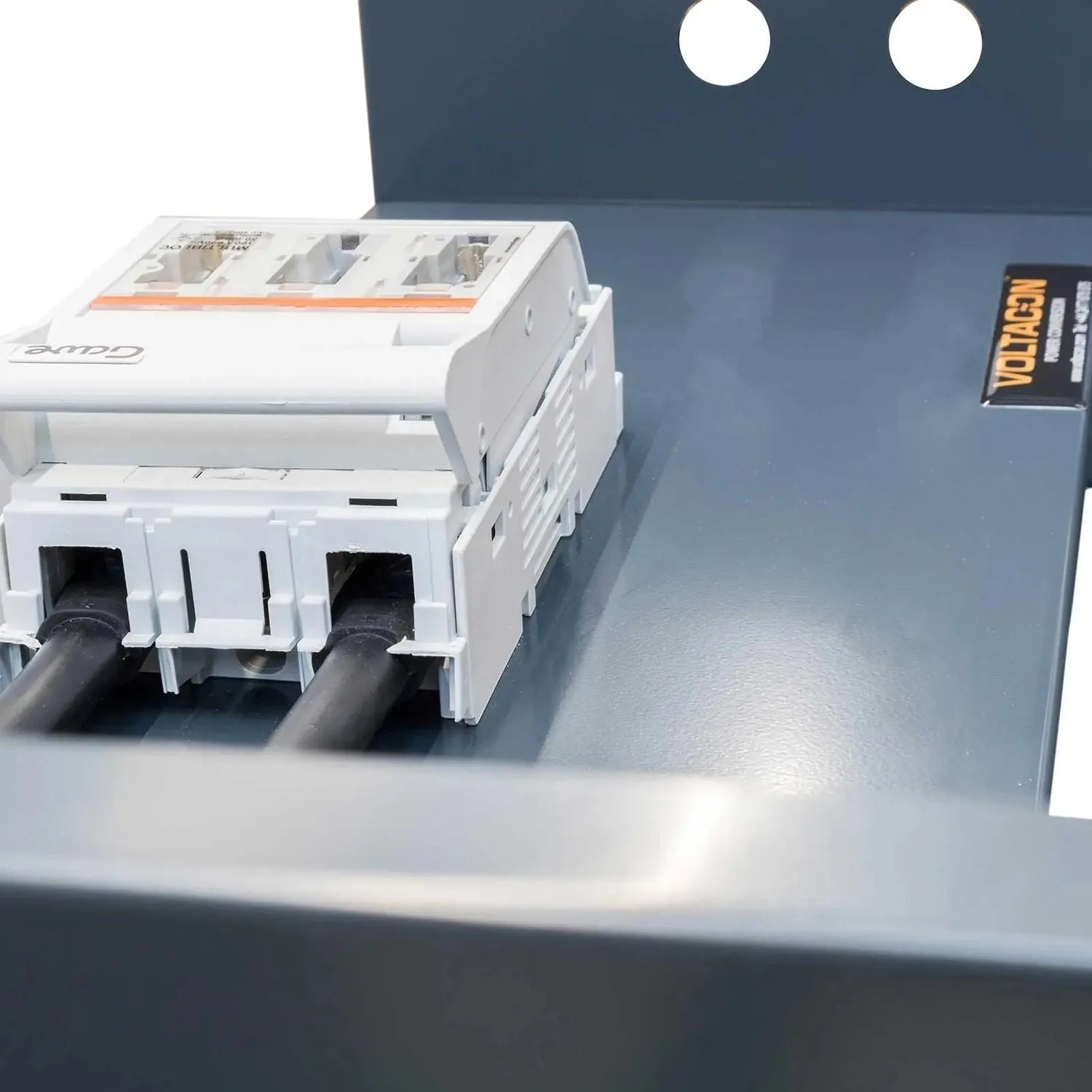 White modular battery storage unit with three compartments mounted on gray surface, with black cables connected and Voltbench