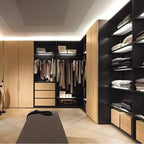 Modern walk-in closet with wood and black cabinetry, illuminated shelves displaying folded linens and clothing on hanging rod