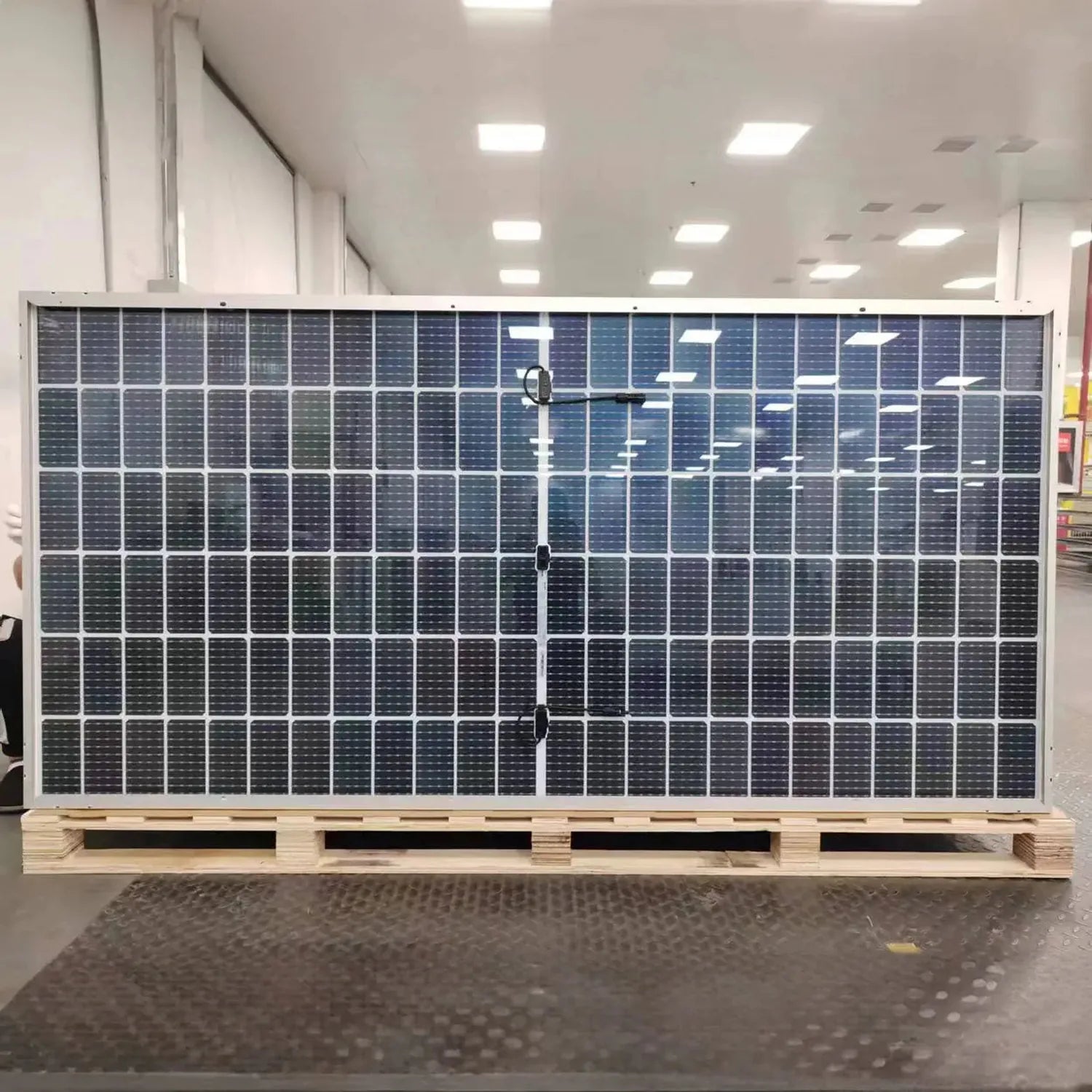 Large solar panel display mounted on wooden pallet in bright indoor showroom with fluorescent ceiling lights.