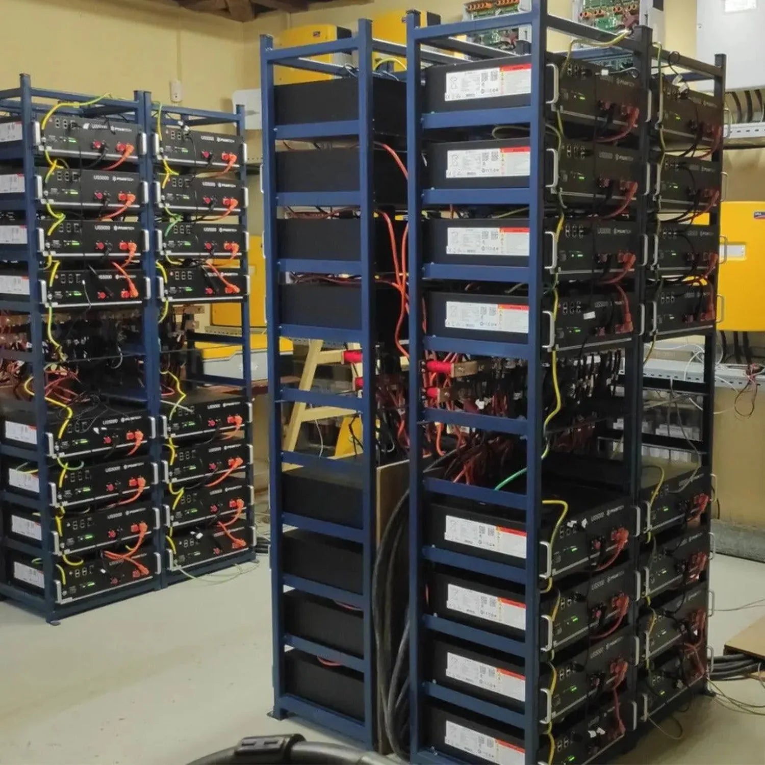 Industrial installation shot showing multiple blue-framed battery cabinets with black power units stacked vertically, display