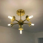 Mid-century modern brass sputnik ceiling light fixture with seven adjustable arms and glowing G9 LED bulbs, mounted on white 