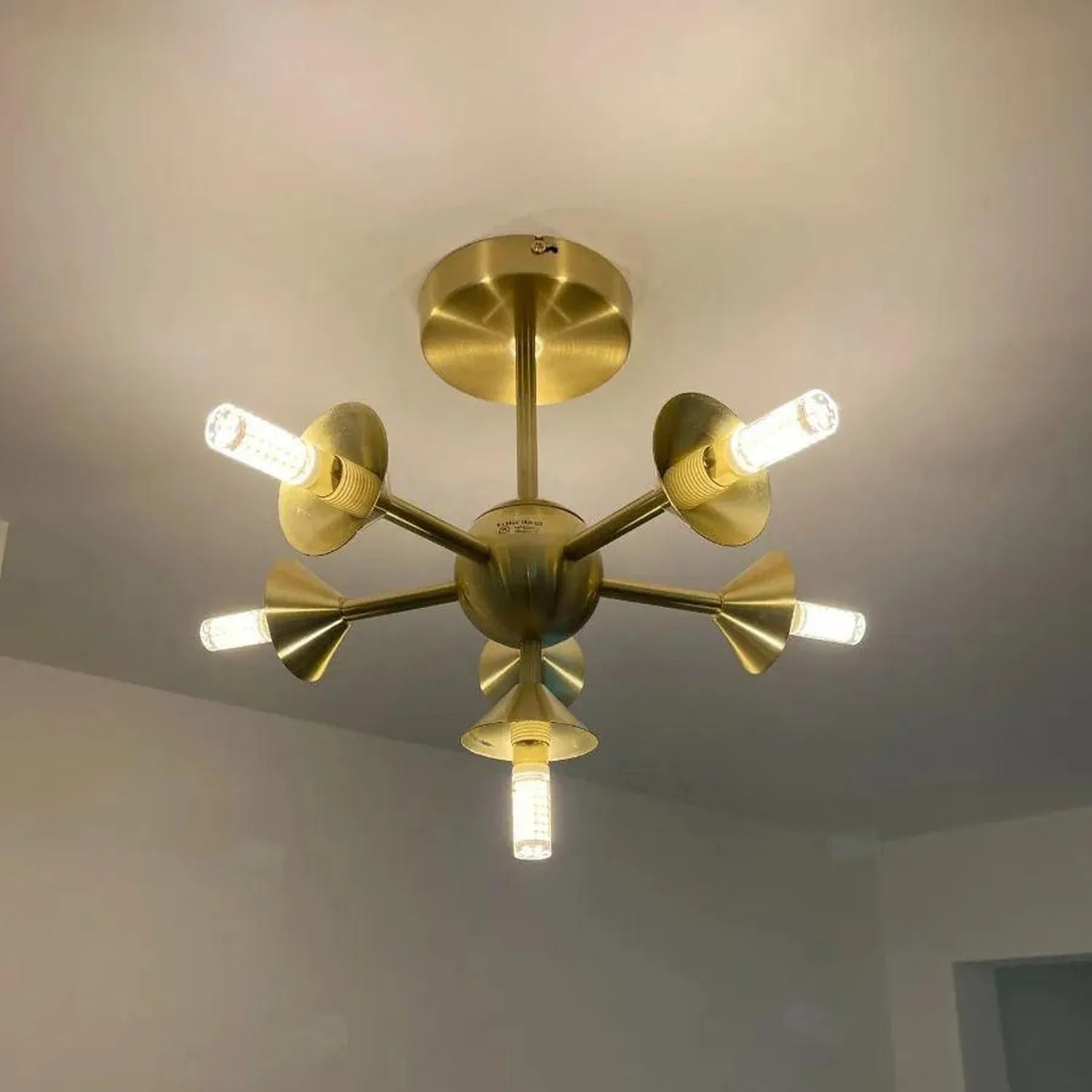 Mid-century modern brass sputnik ceiling light fixture with seven adjustable arms and glowing G9 LED bulbs, mounted on white 