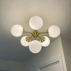 Mid-century modern brass ceiling light fixture with six frosted white glass globe shades installed on white ceiling.