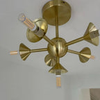 Brass ceiling light fixture with six adjustable cone-shaped arms, each fitted with a G9 LED bulb, mounted on white wall.