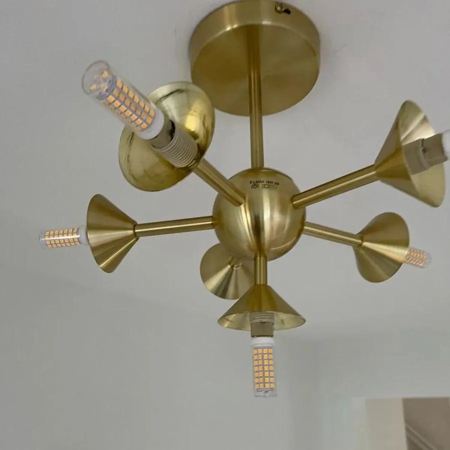 Brass ceiling light fixture with six adjustable cone-shaped arms, each fitted with a G9 LED bulb, mounted on white wall.