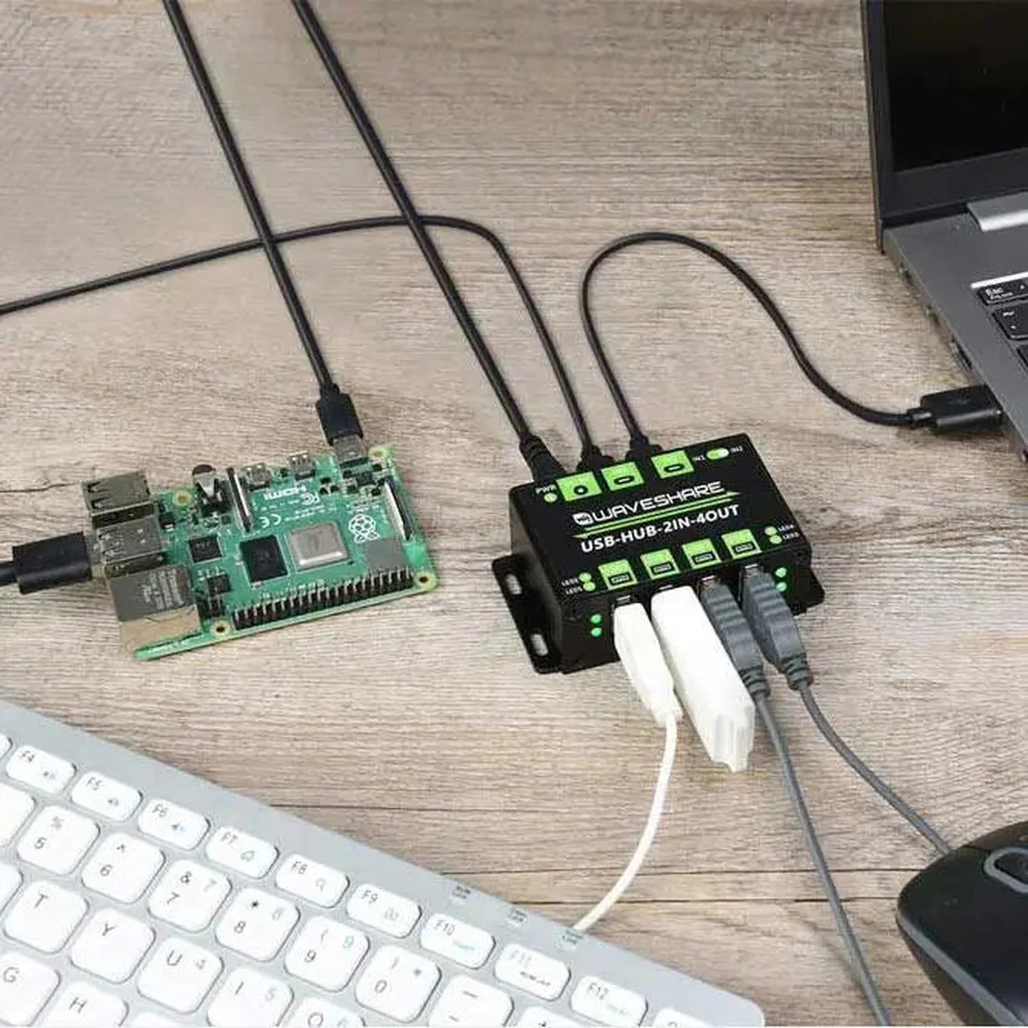 Waveshare USB hub with four ports connected to a Raspberry Pi and laptop on a desk setup with keyboard and mouse.